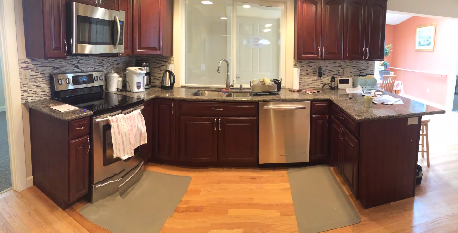 Kitchen with dark wood cabinets, granite countertops, stainless steel appliances (microwave, stove, dishwasher) and a sink facing an interior window.