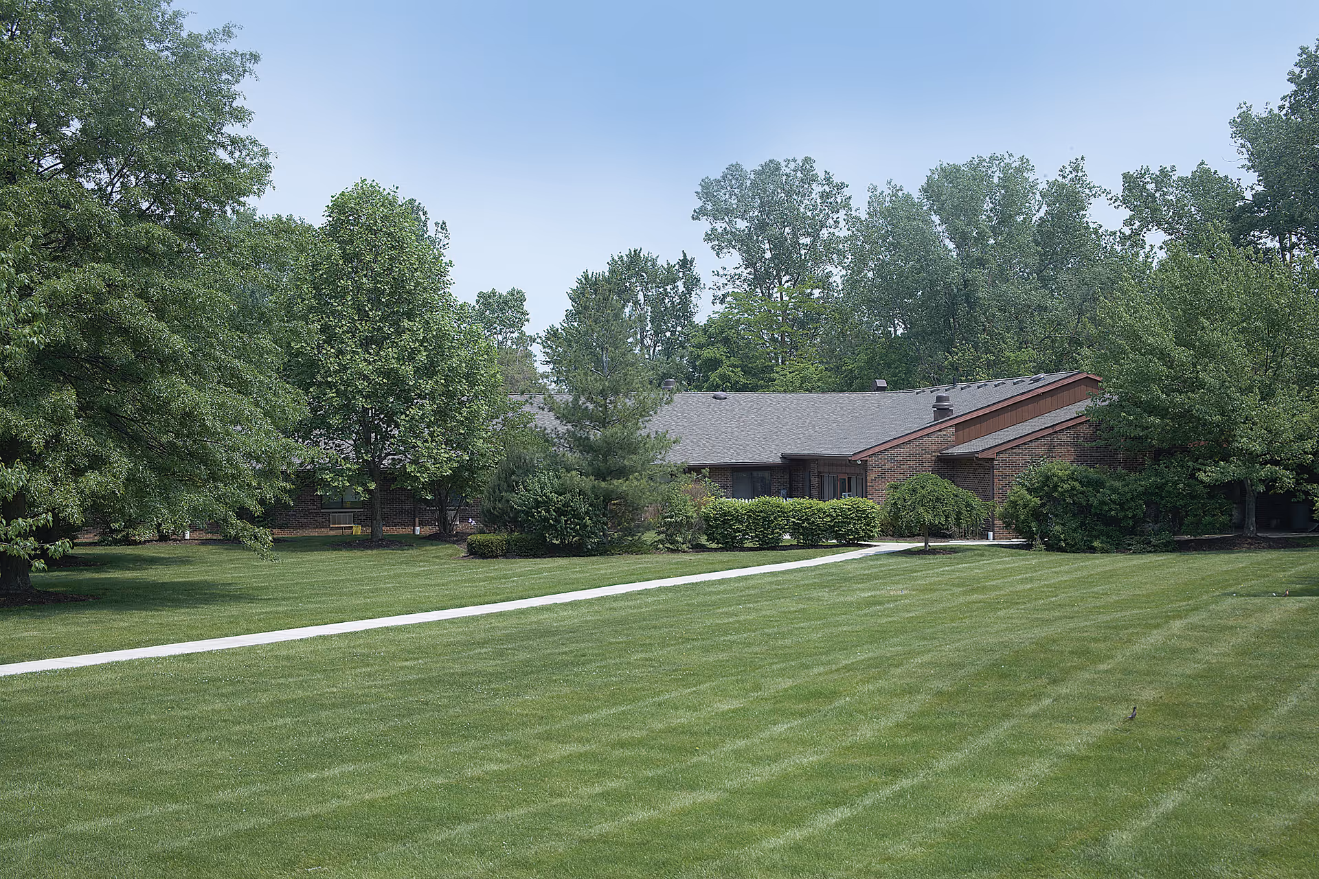 One-story brick building set behind a wide manicured lawn and trees with a walkway leading to the entrance.