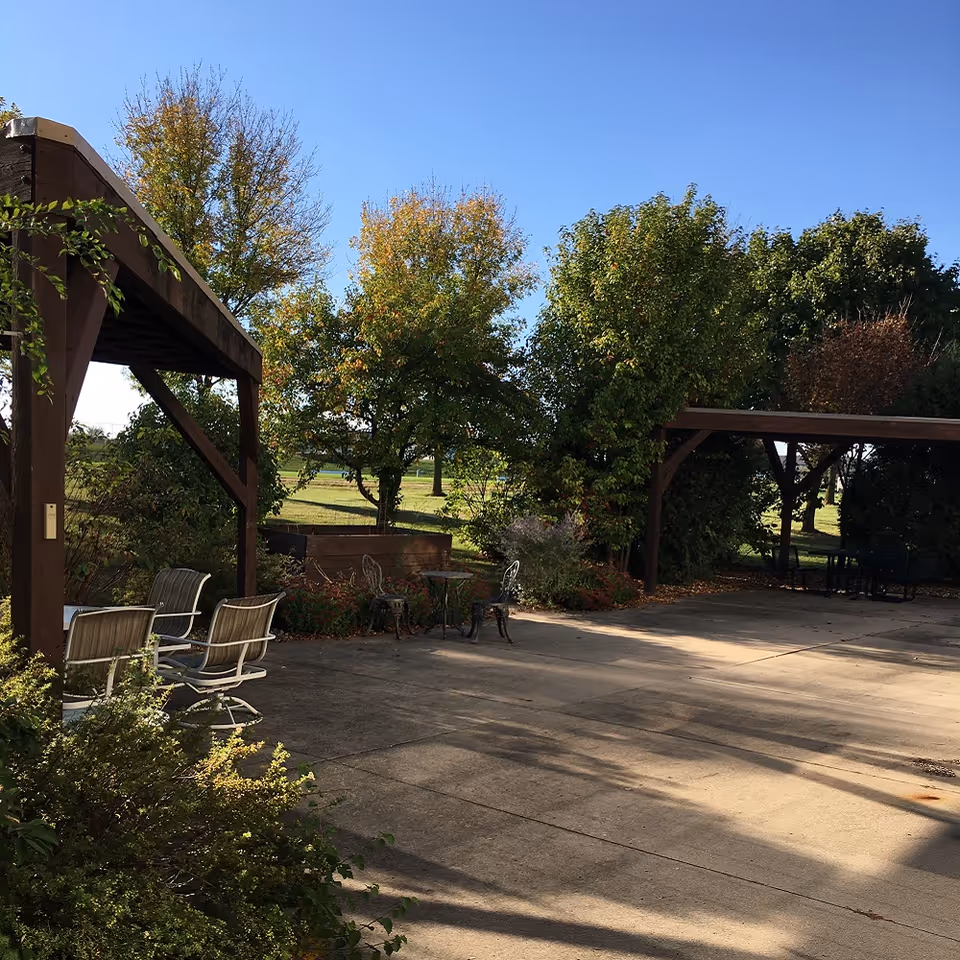 Sunny outdoor courtyard at Ecumen Sand Prairie with wooden pergolas, seating, and trees.