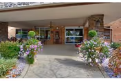 Entrance to Burgess Square Healthcare & Rehab Centre with glass doors, brick facade, and potted flowers.