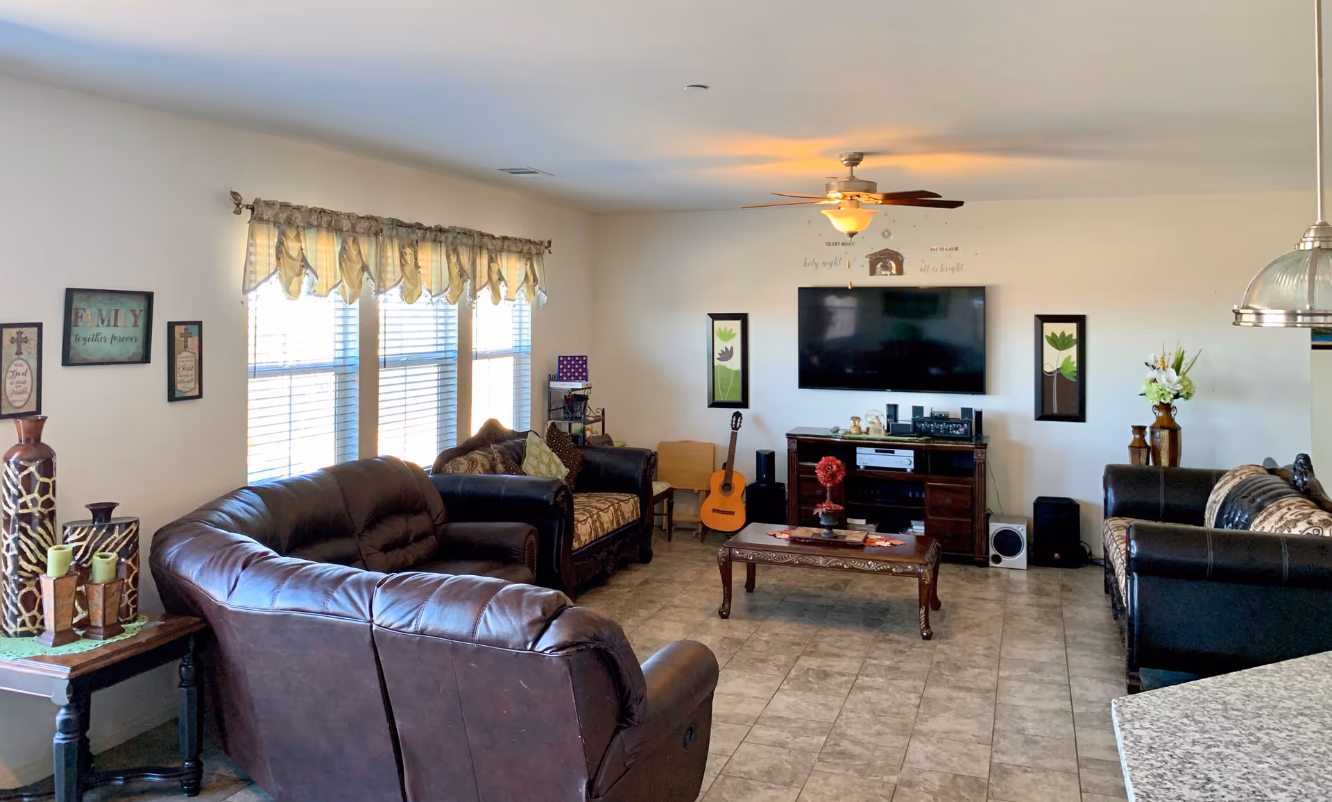 Spacious living room with leather sofas, a coffee table, a wall-mounted TV, and large windows letting in natural light.