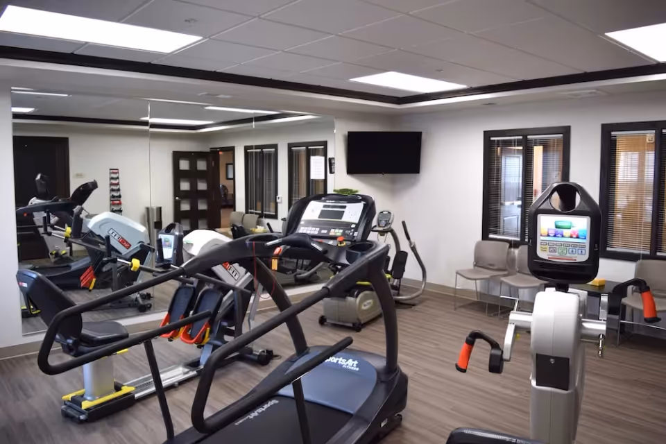 Fitness room with treadmills, exercise bikes, mirrors, a wall-mounted TV and seating.