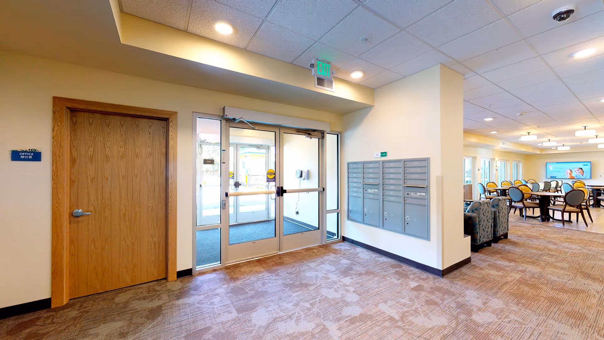 Entrance lobby with glass double doors, wall mailboxes, and a seating/dining area visible to the right.