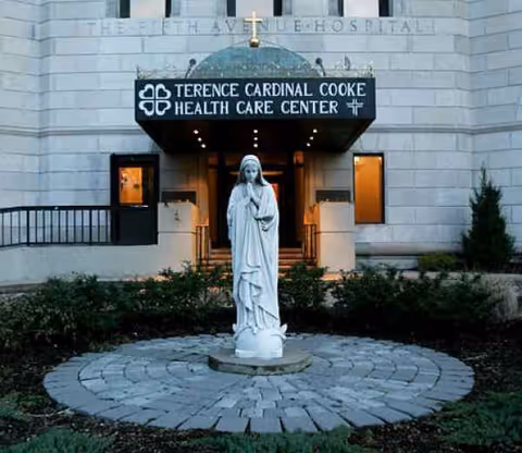 Exterior view of Terence Cardinal Cooke Health Care Center entrance with statue in front.