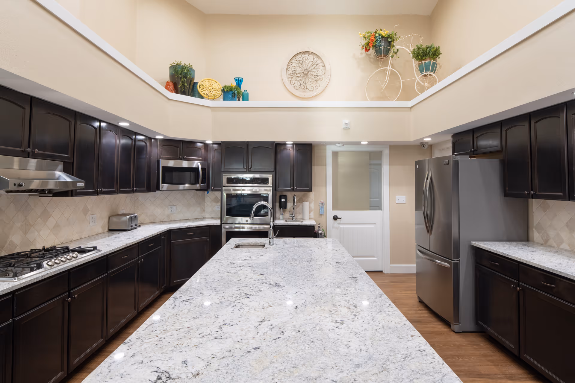 Spacious modern kitchen with a large marble island, dark wood cabinets, and stainless steel appliances.
