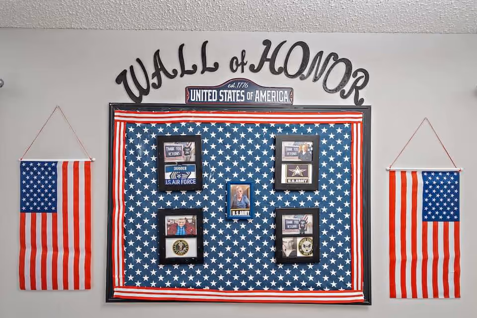 Wall of Honor display featuring a star-spangled backdrop, framed veteran photos and two hanging American flags.