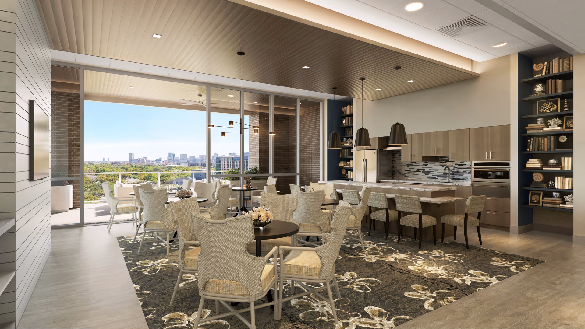 A spacious and modern dining area with multiple round tables surrounded by cushioned chairs. The room features a kitchen area with a large island, bar stools, pendant lighting, and built-in shelves filled with decorative items and books. Large floor-to-ceiling windows provide a view of an outdoor balcony and a cityscape in the distance.