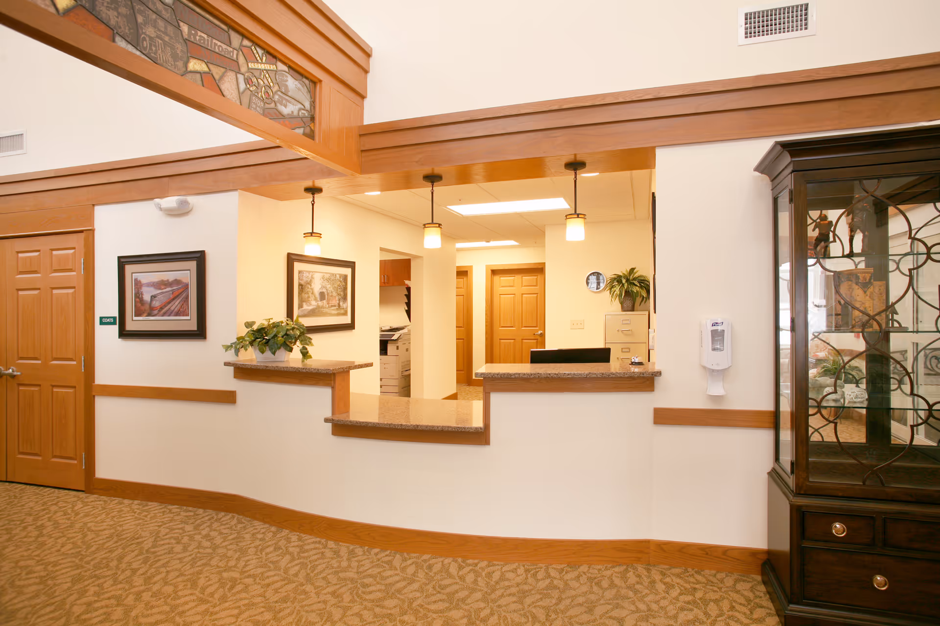 Reception desk and lobby area with wood trim, pendant lights, framed artwork, and a glass display cabinet.