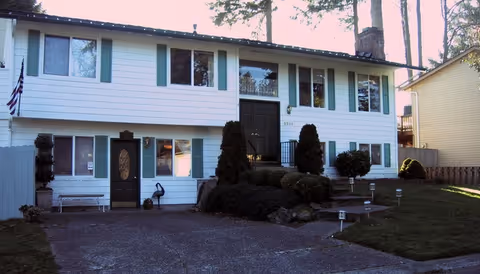 Two-story white house with green shutters, a driveway, and landscaped front yard.