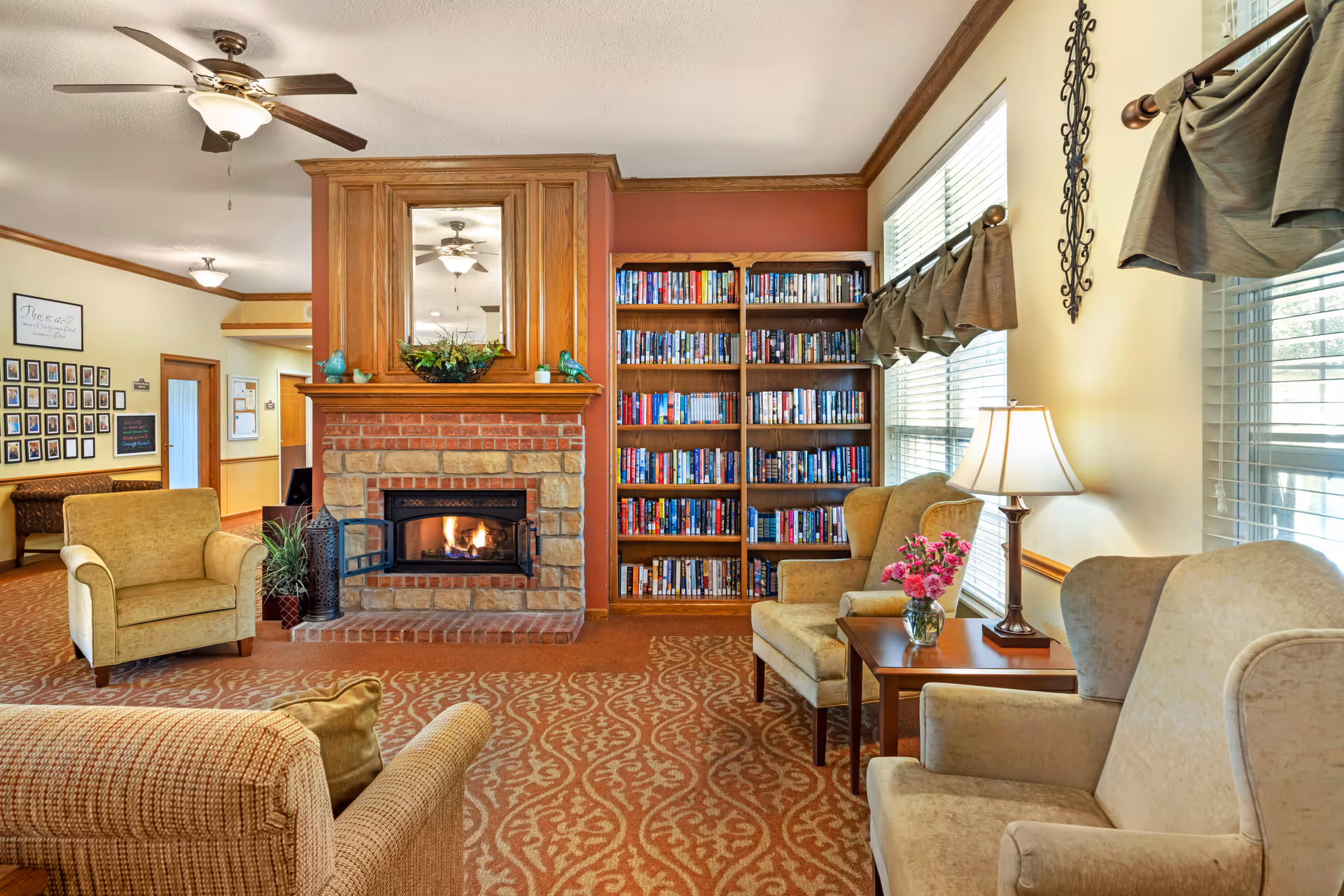 Cozy common room with a stone fireplace, built-in bookshelves, several armchairs, side table and large windows.