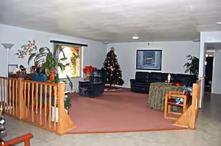 A spacious living room lounge with couches, a Christmas tree, and several potted plants.