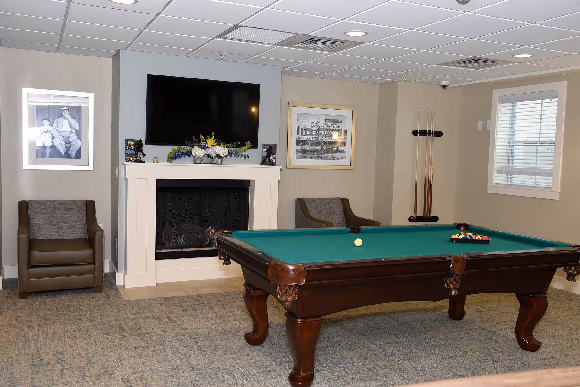 A recreation room featuring a pool table, a fireplace with a mounted TV, chairs, and framed artwork.