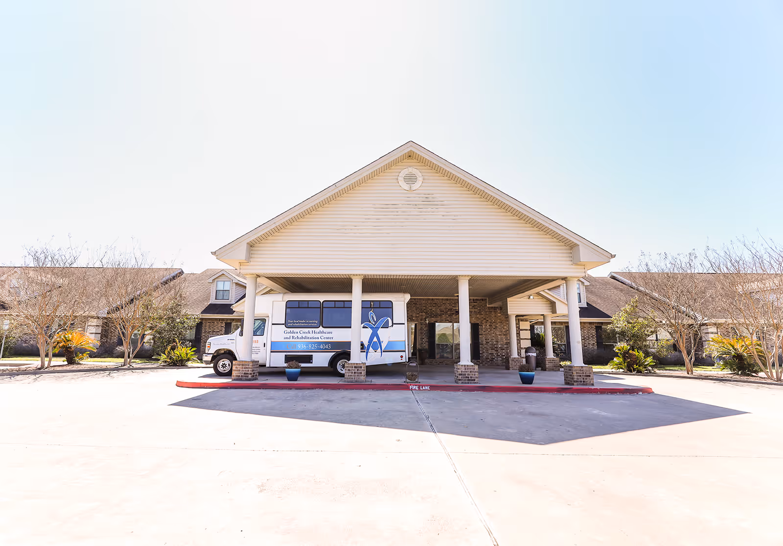 Front exterior view of Golden Creek Healthcare and Rehabilitation Center showing a covered entrance with pillars, a parked shuttle bus, and surrounding landscaping with trees and shrubs.