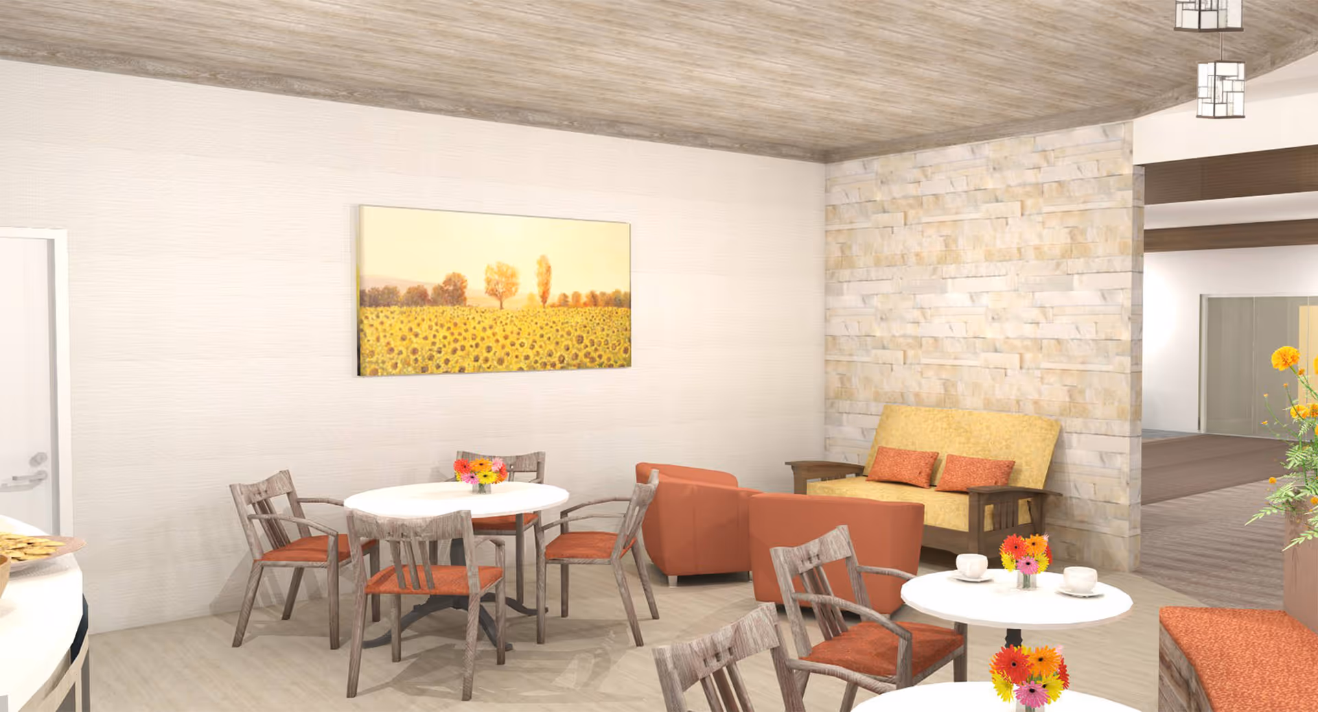 A cozy senior living common area with round tables and wooden chairs featuring orange cushions. There are small flower arrangements on the tables, a yellow cushioned bench with orange pillows, and two orange armchairs. The walls are light-colored with a stone accent wall, and a large painting of a sunflower field hangs on one wall. The ceiling has a wood texture, and pendant lights hang from it.