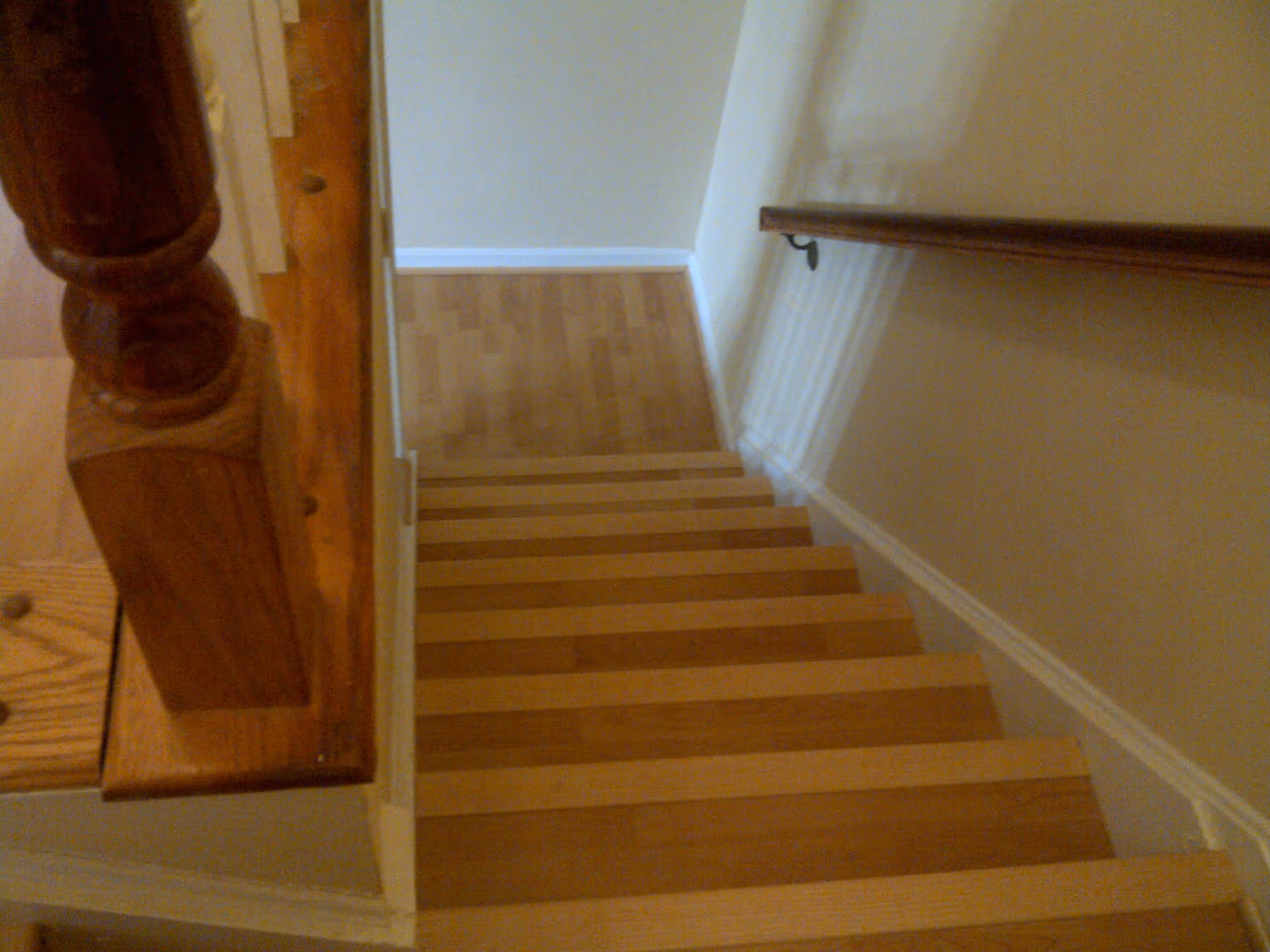 View looking down a wooden staircase with a handrail on the right side and a wooden banister on the left, leading to a landing with wooden flooring and beige walls.
