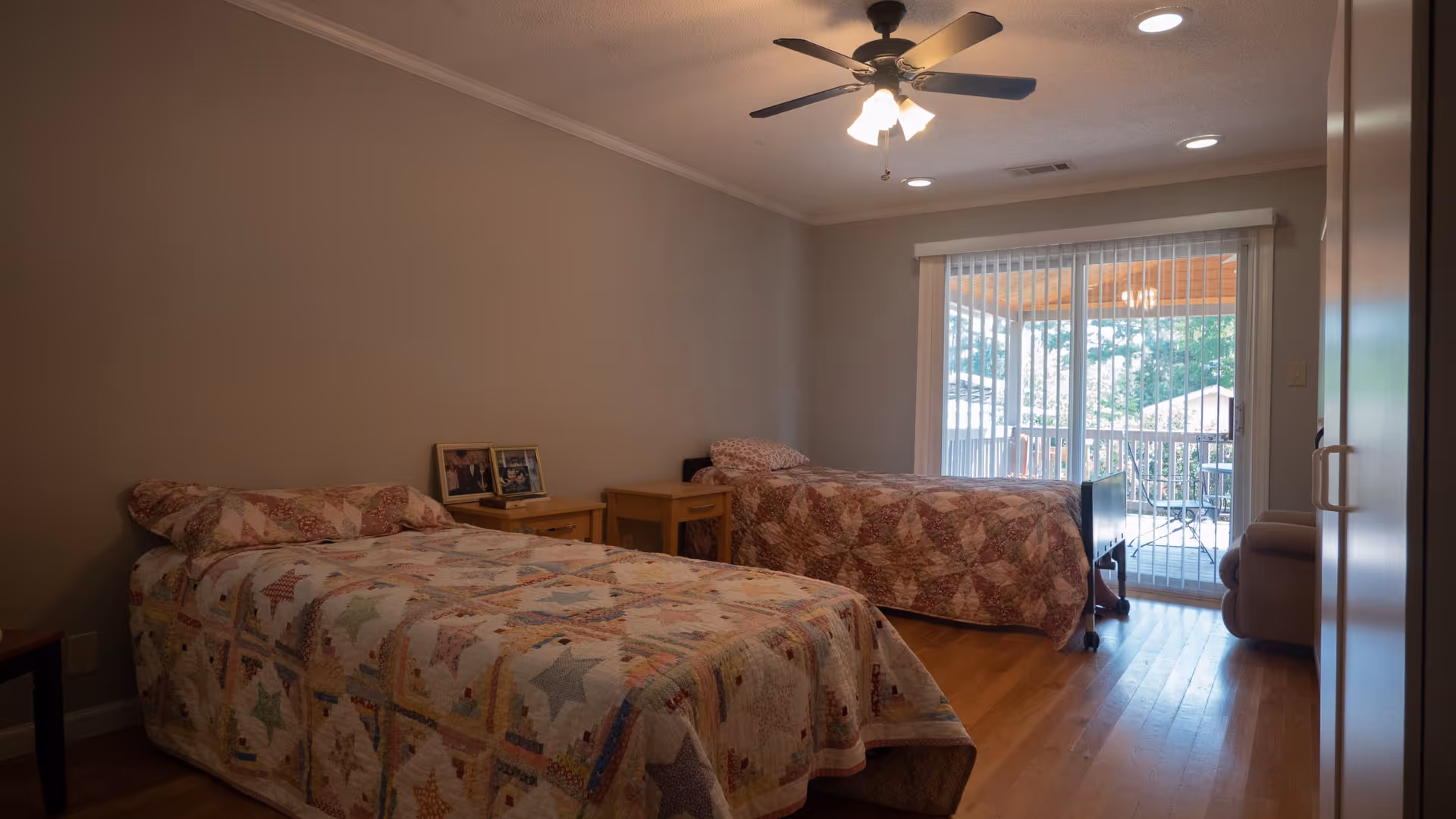 Shared bedroom with two twin beds covered in quilts, a ceiling fan, and a sliding glass door leading to a balcony.