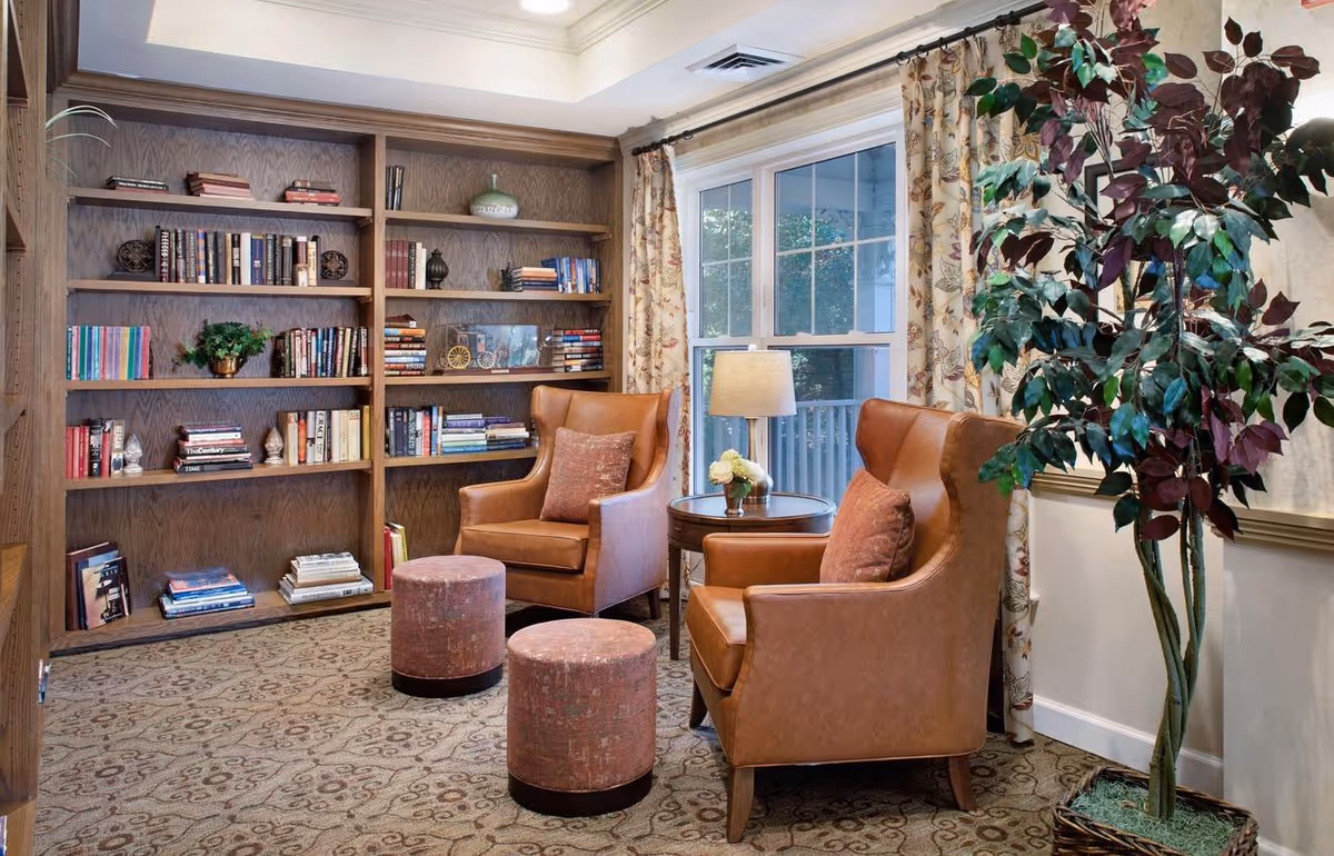 Cozy reading lounge with built-in bookshelves, two leather armchairs, a small round table and potted plant by a window.
