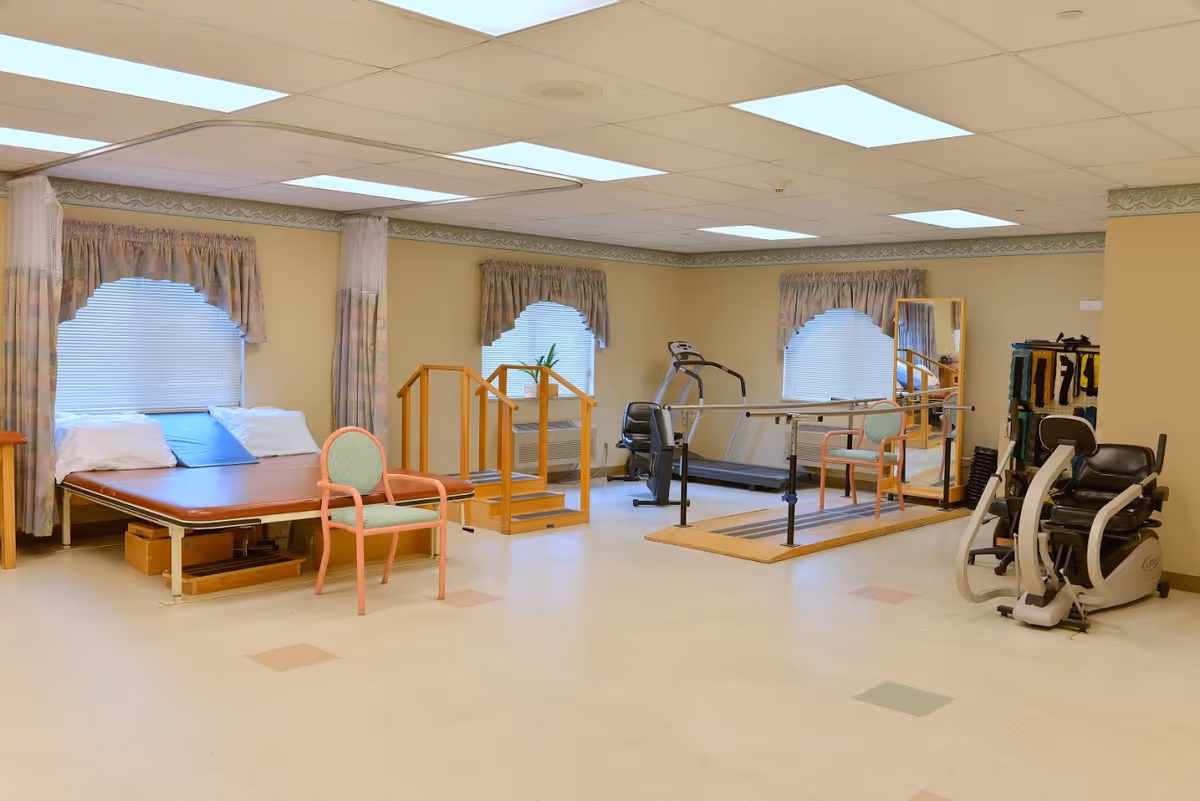Spacious senior rehabilitation room with a treatment table, parallel bars, treadmill, exercise machines and chairs.