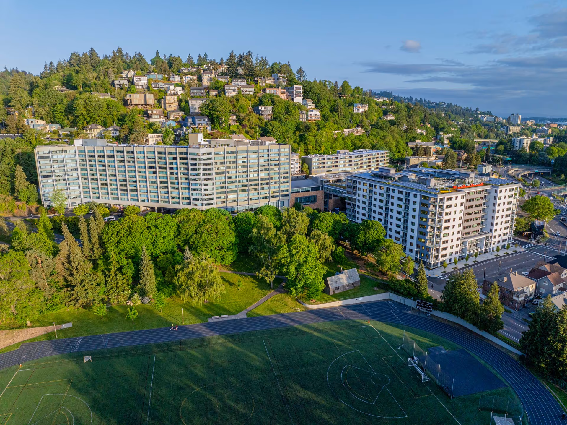 An aerial view of Terwilliger Plaza's hillside campus with multiple buildings and a central sports field.