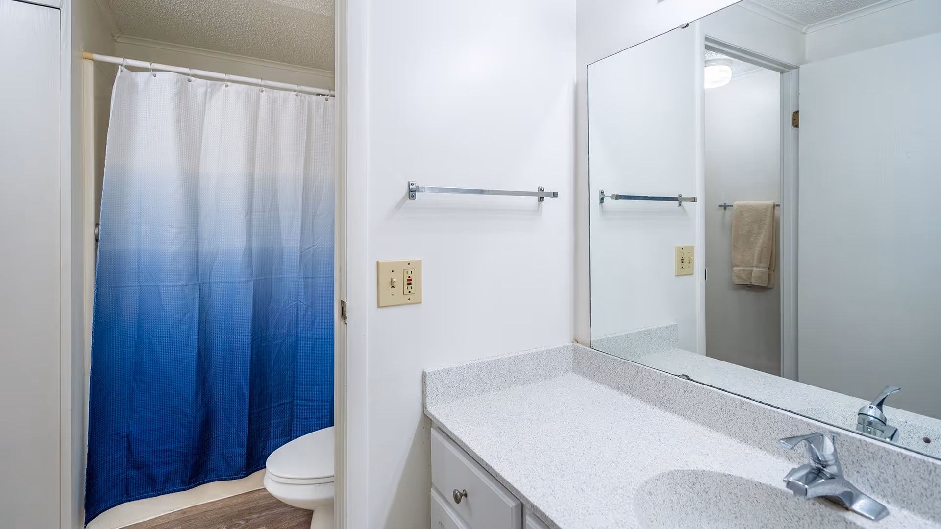 Bathroom with a sink and countertop, large mirror, towel rack, and a shower with a blue ombre curtain.