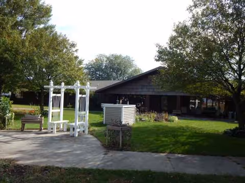 Exterior view of Sheffield Care Center with lawn, walkway, and a white garden arch.