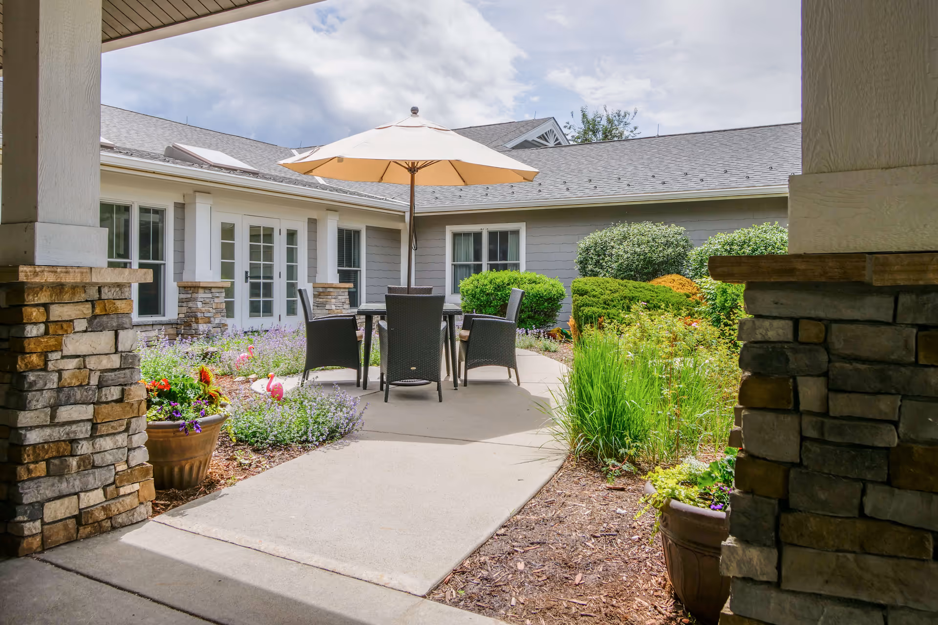 Courtyard patio with a table, chairs and umbrella surrounded by plants and the building exterior.