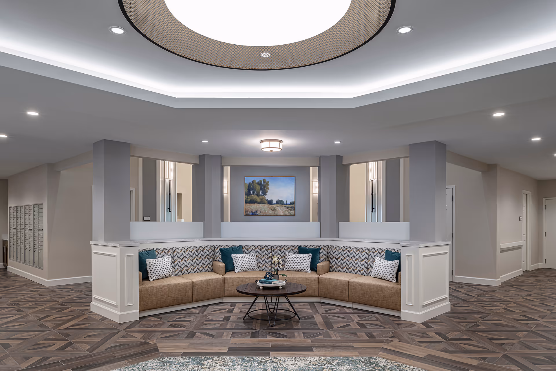 A modern lobby lounge with a curved cushioned bench around a round coffee table under recessed ceiling lighting.