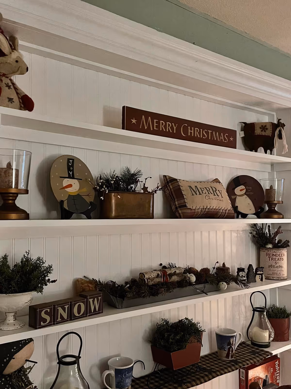 White built-in shelves decorated with Christmas signs, pillows, greenery, and seasonal ornaments.
