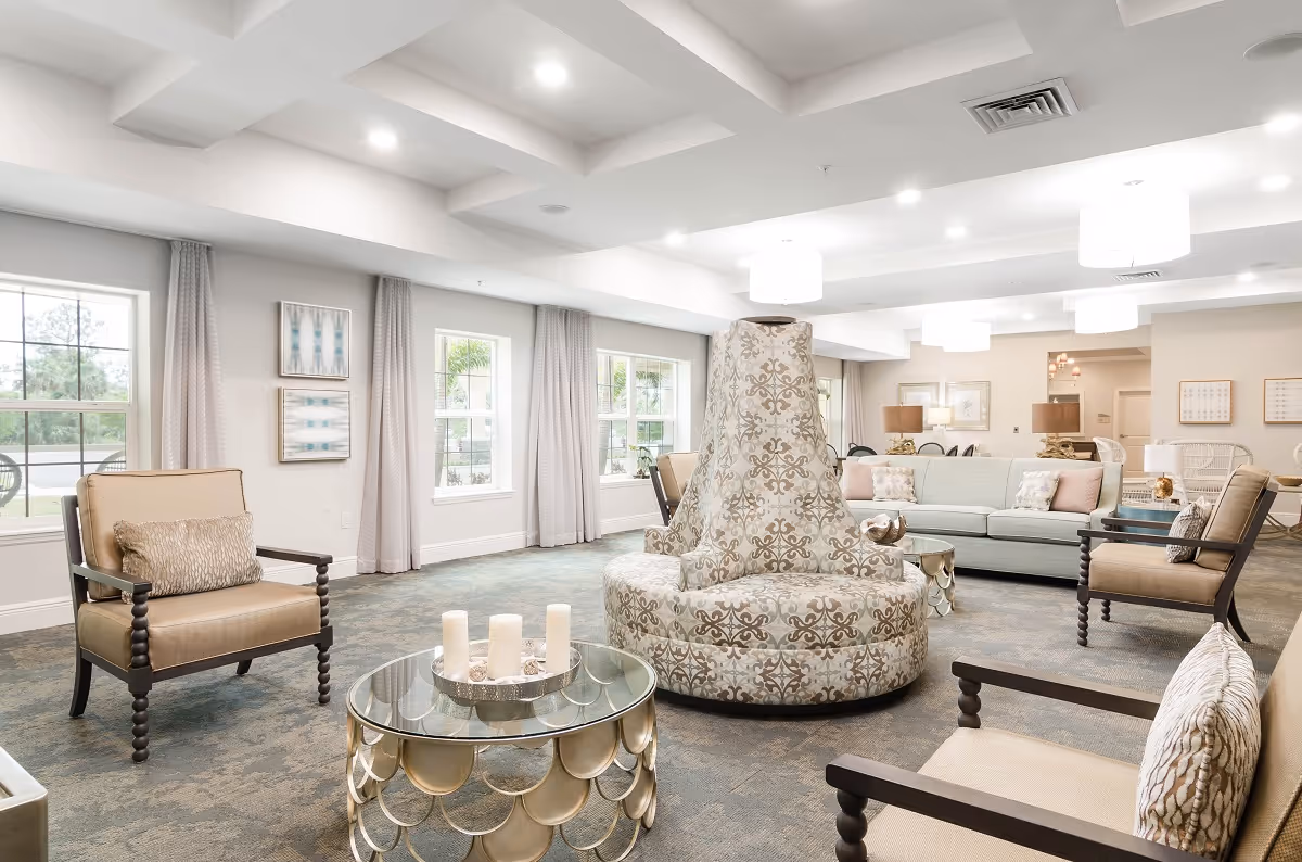 Bright, spacious lounge with multiple armchairs and sofas arranged around a patterned central circular seating piece and a glass coffee table with candles.