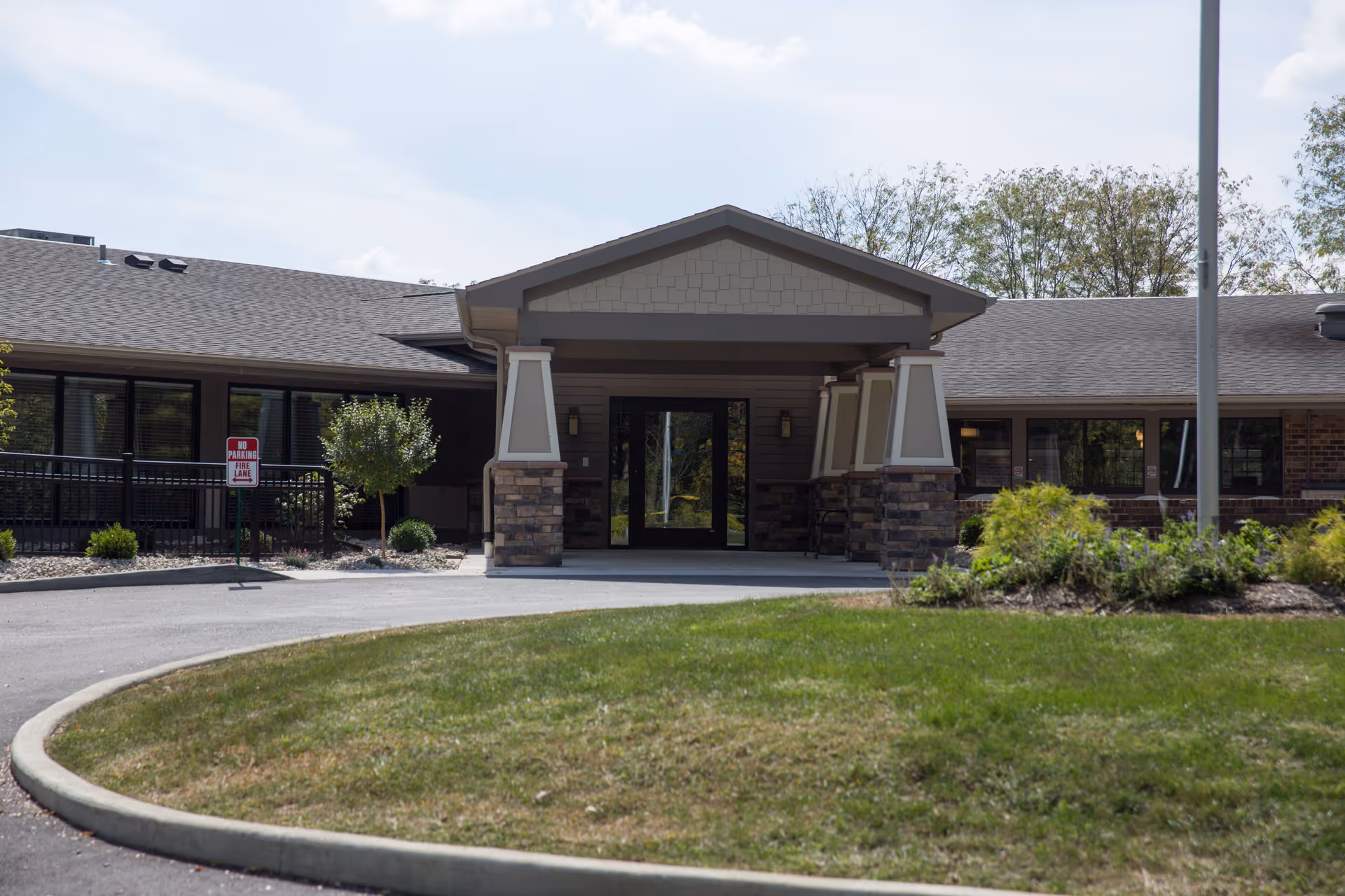 Front exterior view of Shawnee Manor building with a covered entrance supported by stone and beige pillars, surrounded by a curved driveway and landscaped greenery.