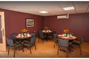 Small dining room with four round tables set for meals, chairs, wood floor and maroon-colored walls.