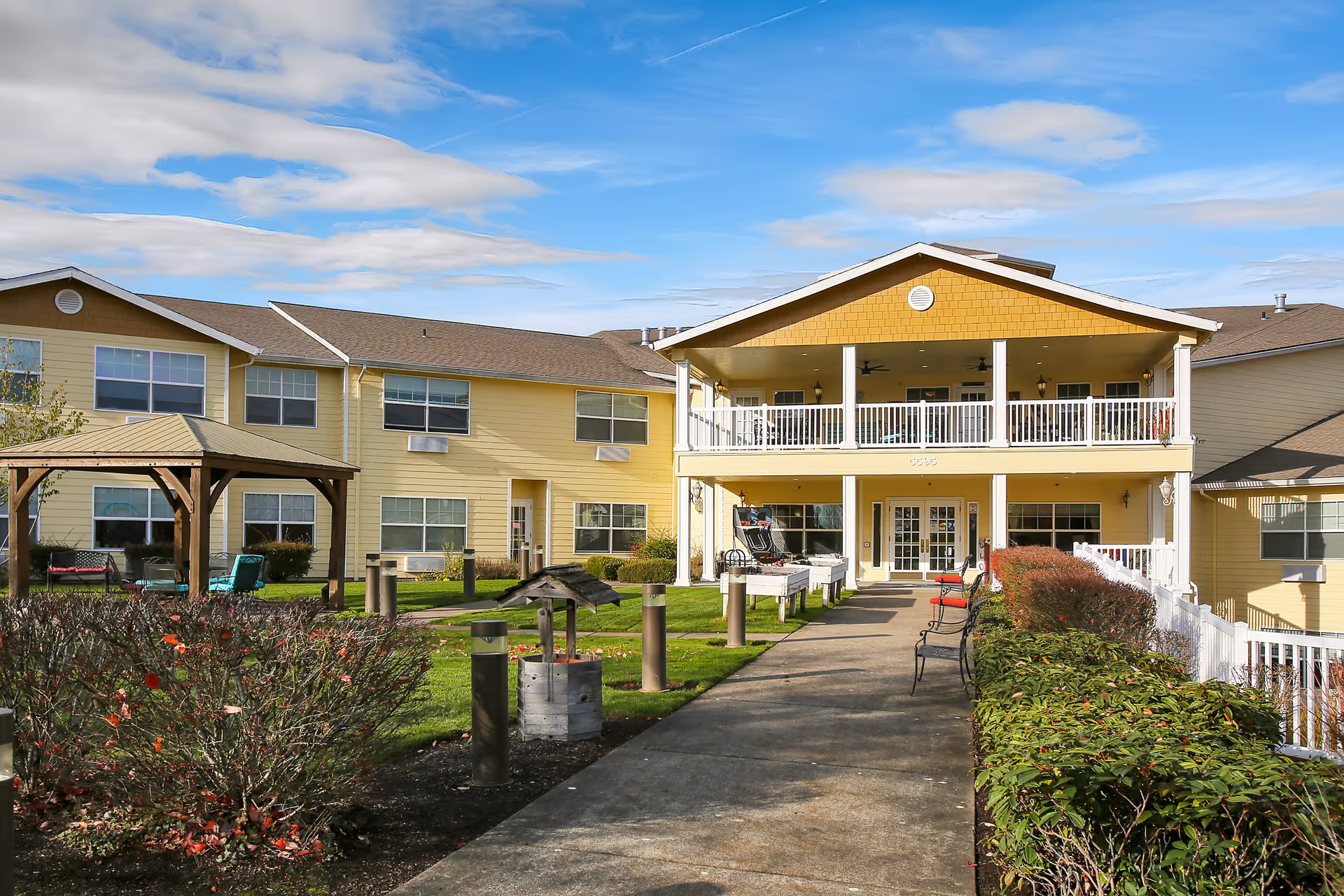 Exterior view of Prestige Senior Living West Hills with a yellow building and outdoor seating.