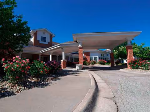 Red brick senior living facility with a covered entrance and landscaped shrubs.