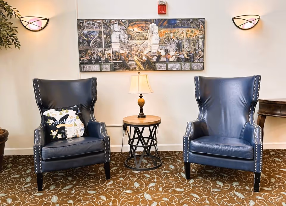 Two navy leather wingback chairs flank a round accent table with a lamp beneath a framed artwork in a cozy seating area.