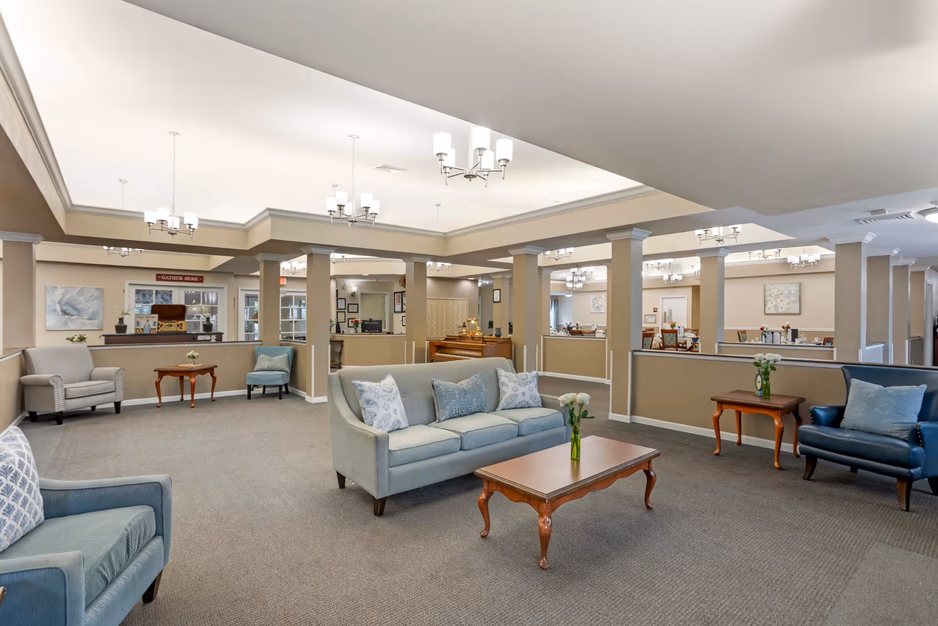 Spacious senior living lounge with sofas, armchairs, coffee tables, and columns under recessed ceiling lighting.