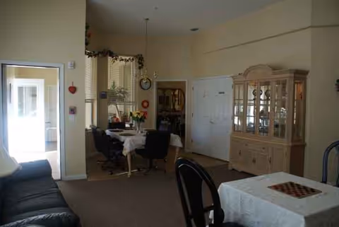 Light-filled dining area in a senior living facility with tables, chairs, and a glass china cabinet.