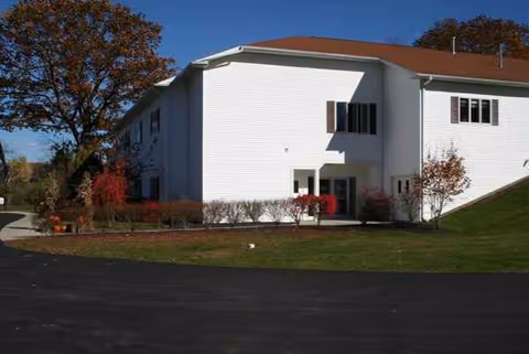 White senior living building with entrance and surrounding landscaping.