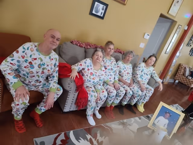 Five people in matching festive pajamas sitting together on and beside a couch in a living room.