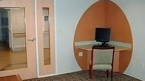 Corner of a pastel blue interior with an oval wooden alcove desk and computer.