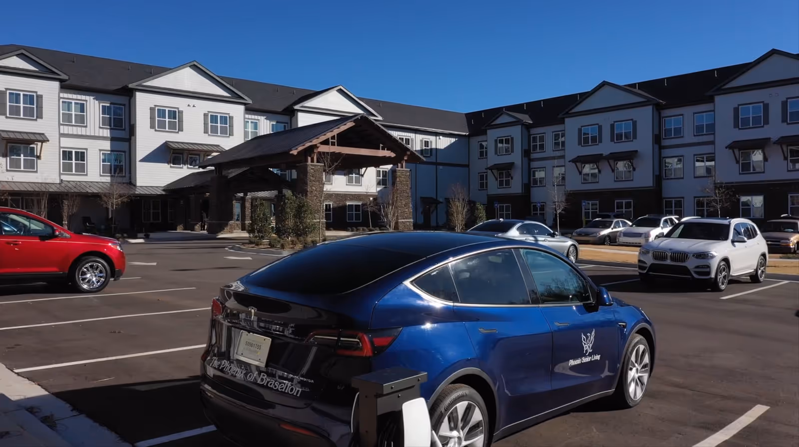 Blue sedan in foreground with senior living building and parking lot in daylight.
