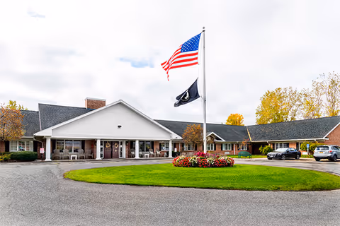 Exterior view of Elderwood Village at Fairport entrance with flags and flower bed.