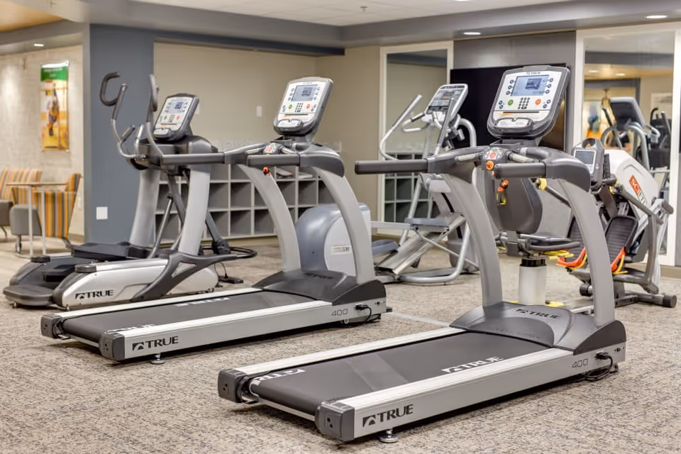 Fitness room with multiple treadmills and other exercise machines facing a mirrored wall and seating area.