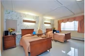 Two twin beds in a shared patient room with pastel decor.