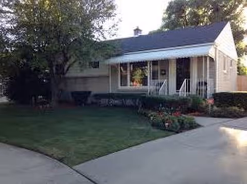 Single-story, house-like senior living facility with a front porch and landscaped yard.