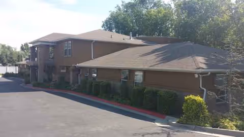 Exterior view of a brown single-story senior living facility with trimmed hedges.