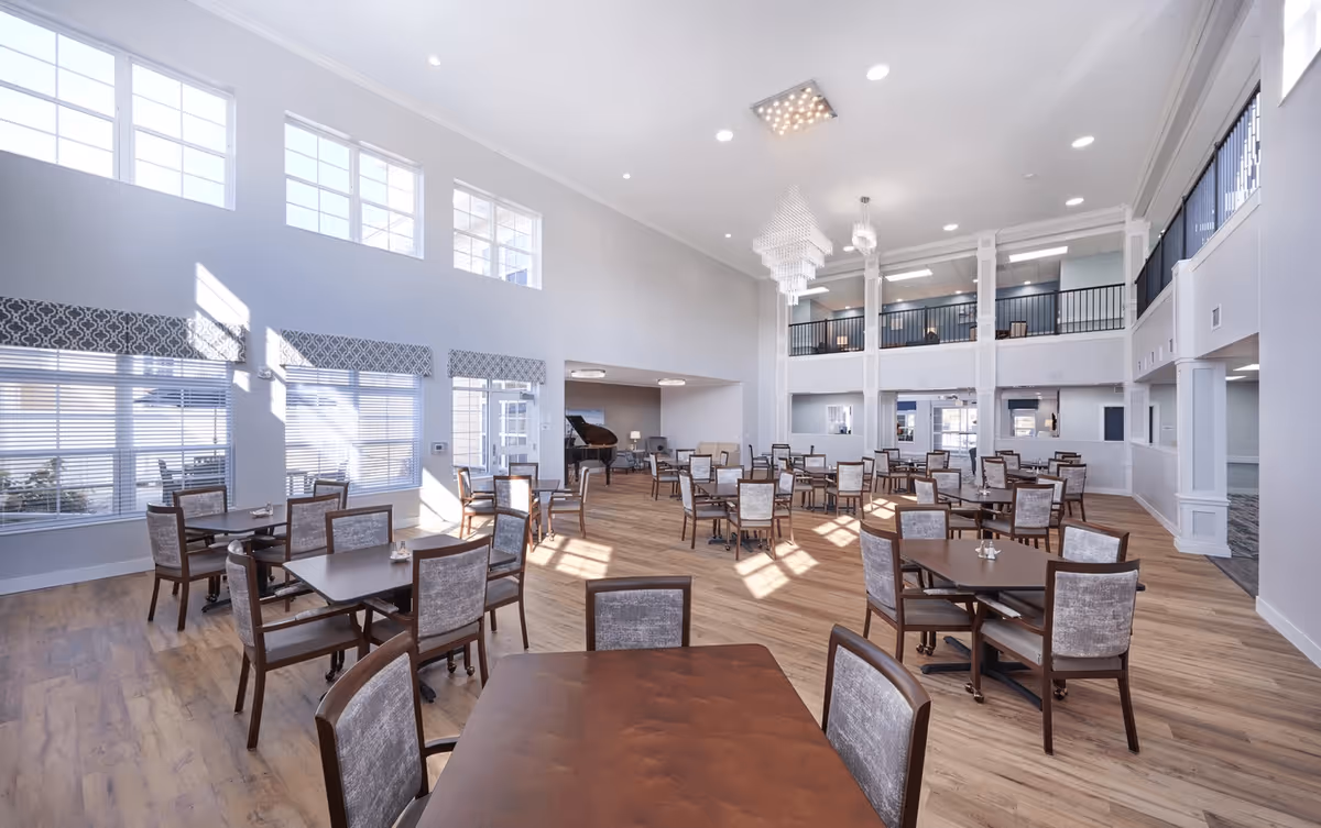 Bright, spacious dining room with multiple dining tables and chairs, high ceilings, a mezzanine balcony and large windows.