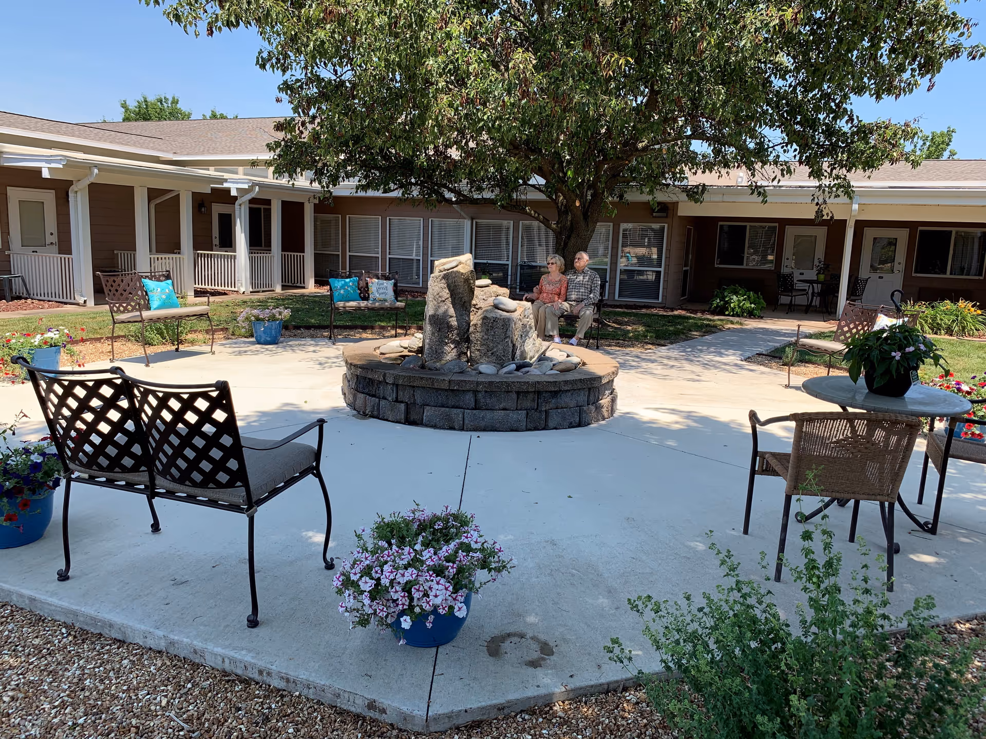 Outdoor courtyard at The Gardens with benches, a fountain, and residents seated nearby.