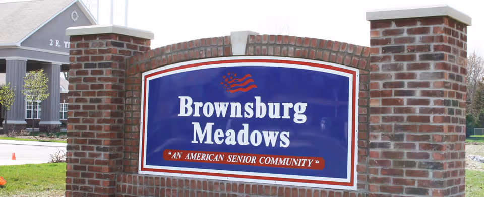 Brick entrance sign reading "Brownsburg Meadows" with the tagline "An American Senior Community" and the facility building visible behind it.