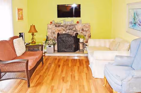 Cozy living room with lime-green wall, stone fireplace, TV, and several chairs.