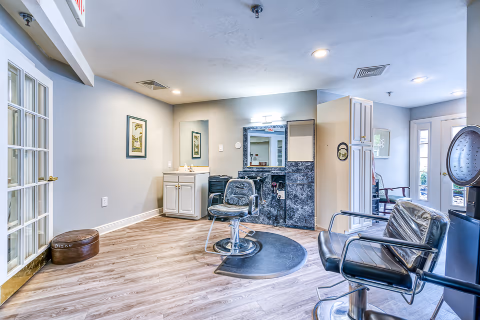 Bright interior salon area with styling chairs, mirrors, and cabinets in a senior living facility.